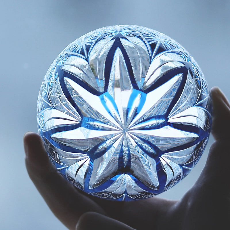 Hand holding a crystal whiskey glass with intricate starburst cut design and blue accents