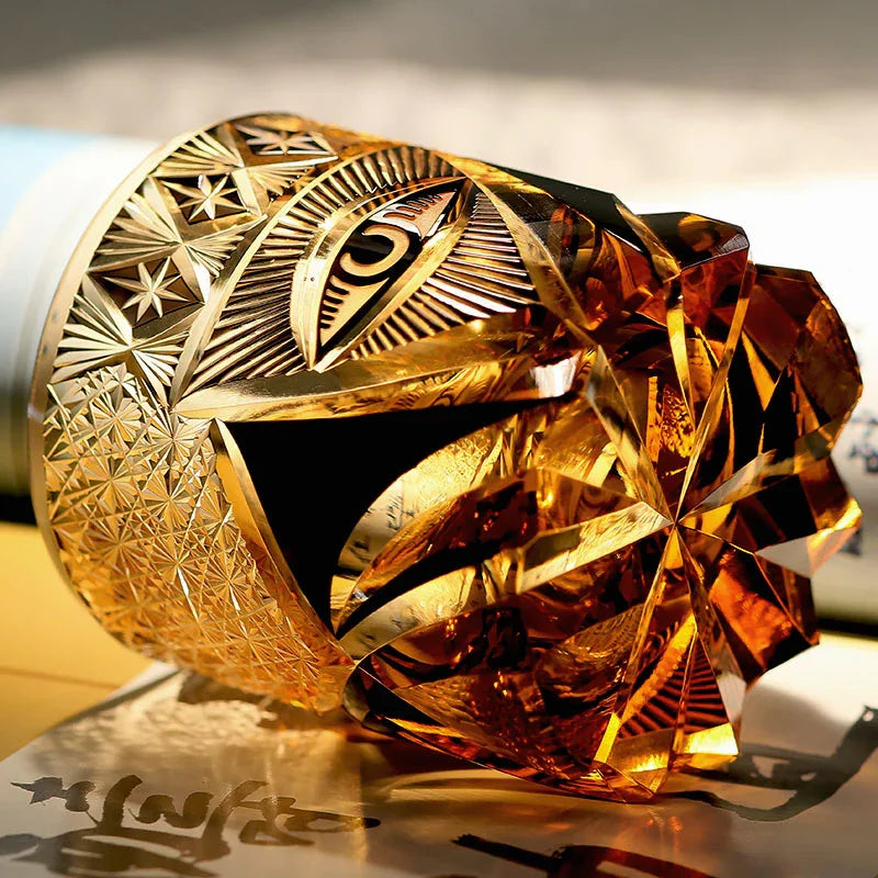 Hand cut crystal whiskey glass with intricate geometric and eye engravings in amber hues
