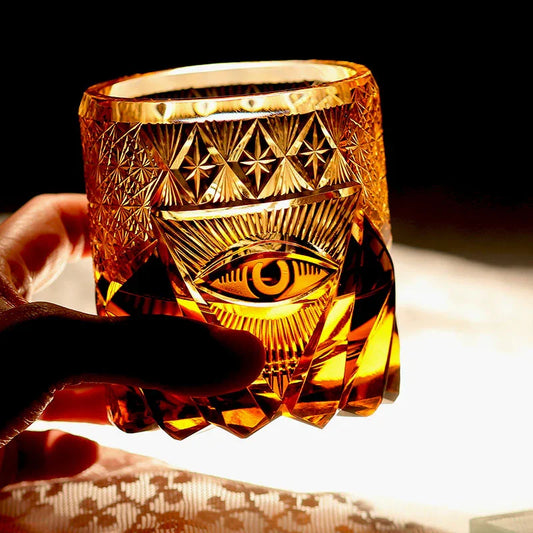 Hand holding a hand cut crystal whiskey glass with engraved eye and geometric patterns