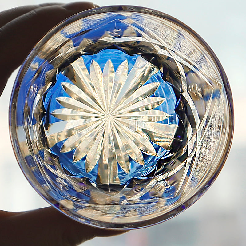 Hand holding a cut crystal whiskey glass with intricate starburst pattern and blue accents