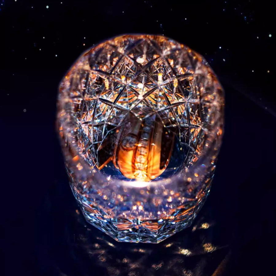 Hand cut crystal whiskey glass with intricate facets reflecting amber liquid on dark background