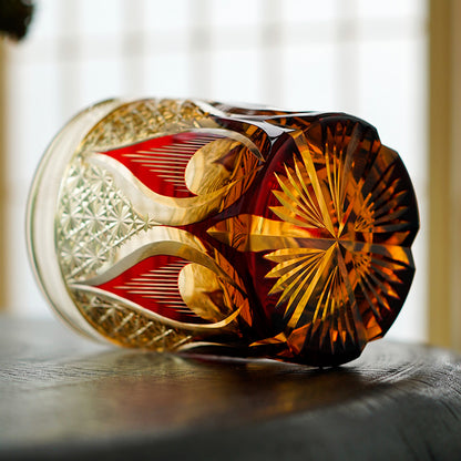 Hand cut crystal whiskey glass with intricate red and gold patterns, lying on its side