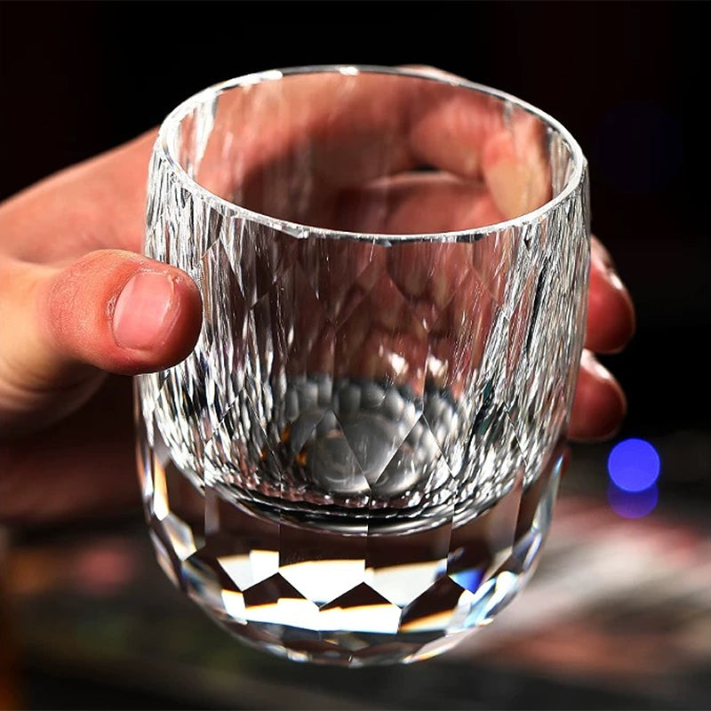Hand holding a hand-cut crystal whiskey glass with detailed faceted pattern.