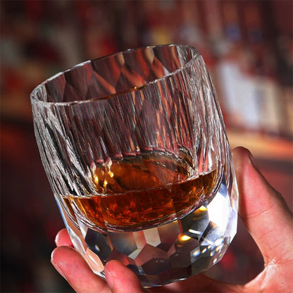 Hand holding a crystal whiskey glass with geometric cut facets and amber liquid