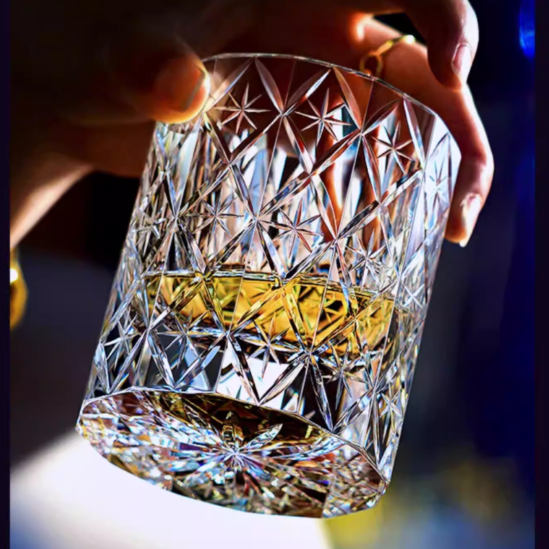 Hand holding a hand cut crystal whiskey glass with amber liquid, showcasing intricate facets