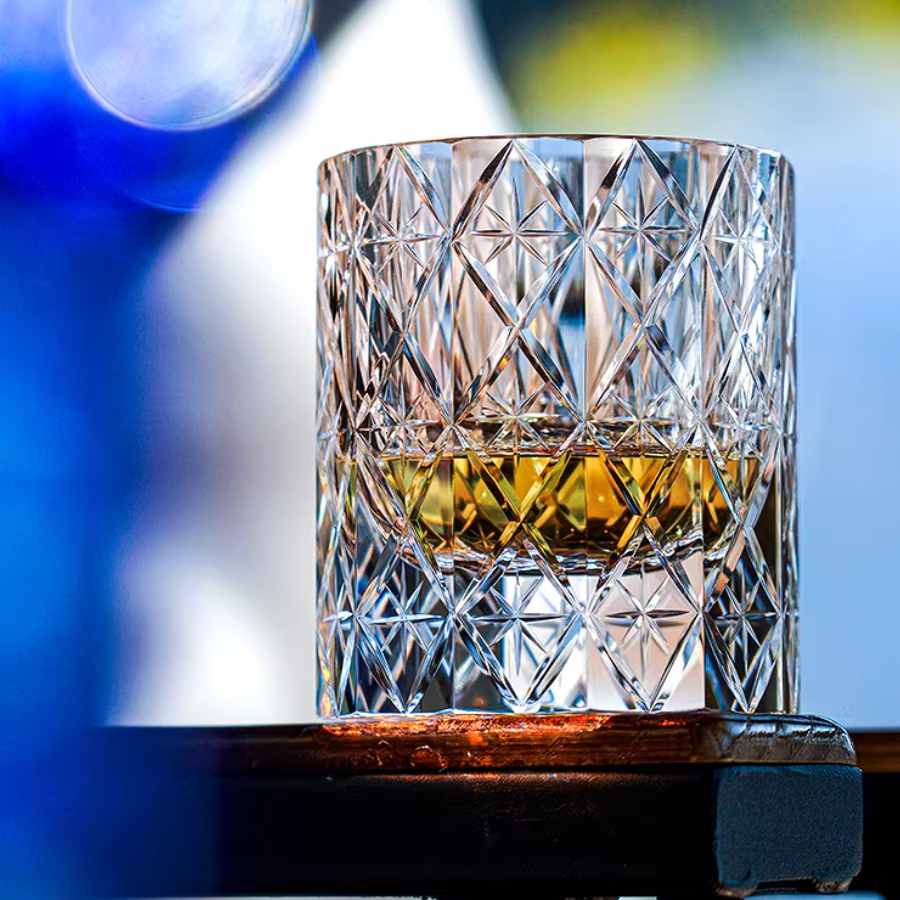 Hand cut crystal whiskey glass with intricate facets and amber liquid, close-up shot