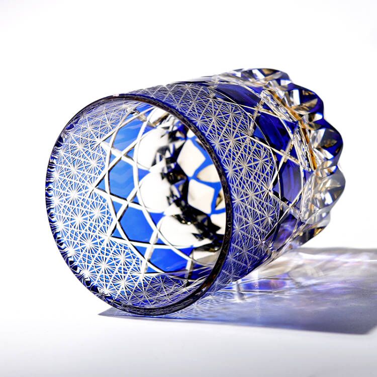 Blue hand cut crystal whiskey glass with geometric pattern, lying on its side