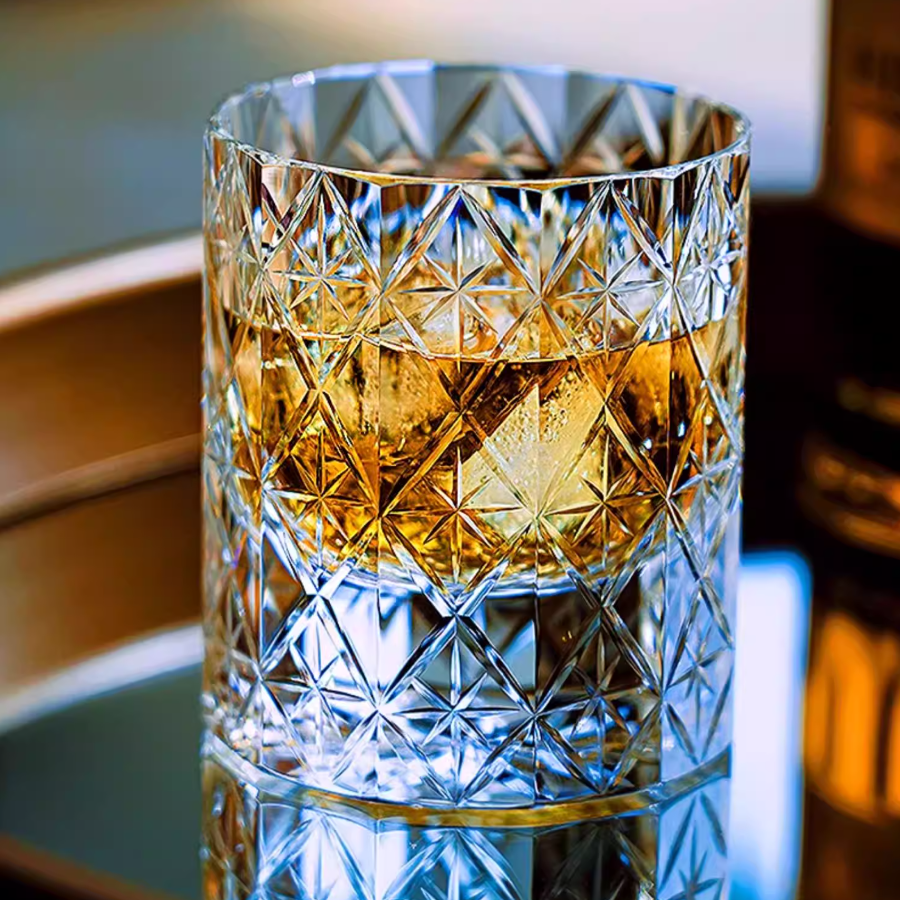 Hand cut crystal whiskey glass with geometric facets, filled with whiskey and ice