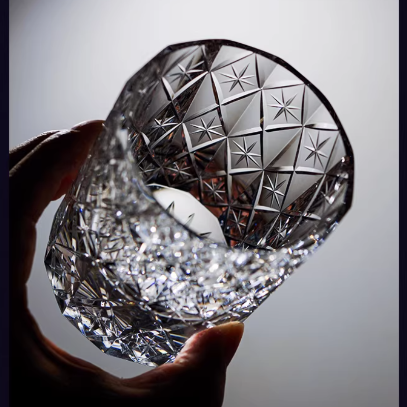 Hand holding a cut crystal whiskey glass with star-patterned facets and sparkling detail