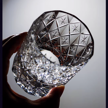 Hand holding a cut crystal whiskey glass with star-patterned facets and sparkling detail
