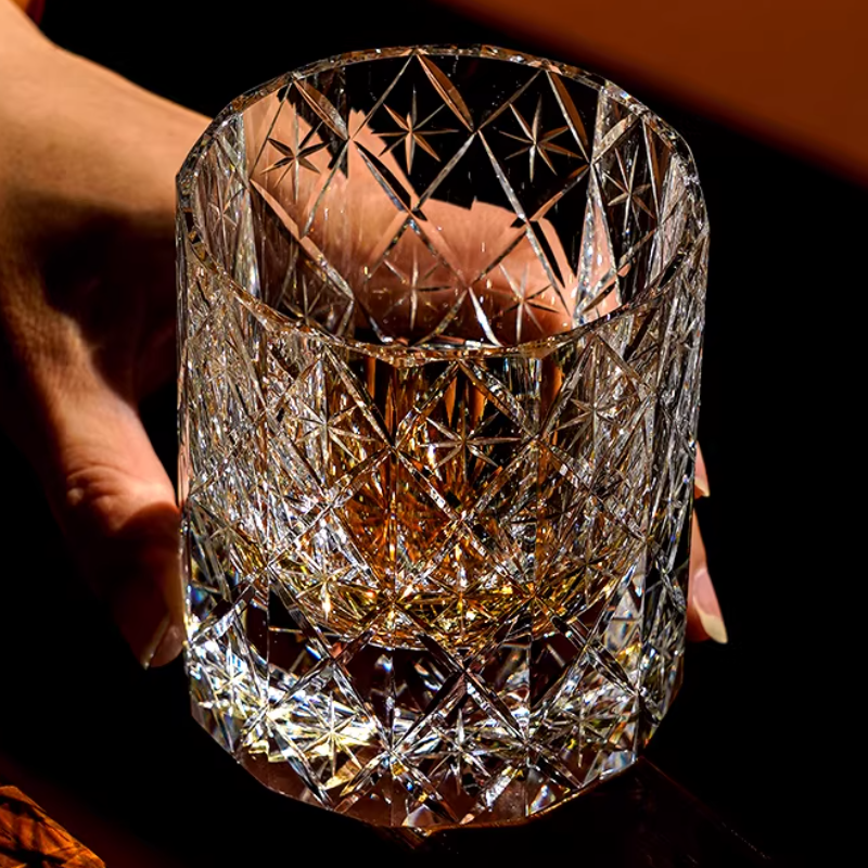 Hand holding a hand cut crystal whiskey glass with intricate facets, filled with whiskey