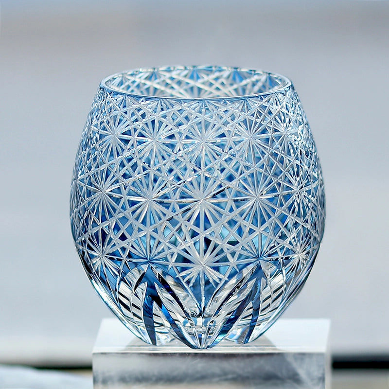 Hand cut crystal whiskey glass with intricate geometric facets on a reflective surface