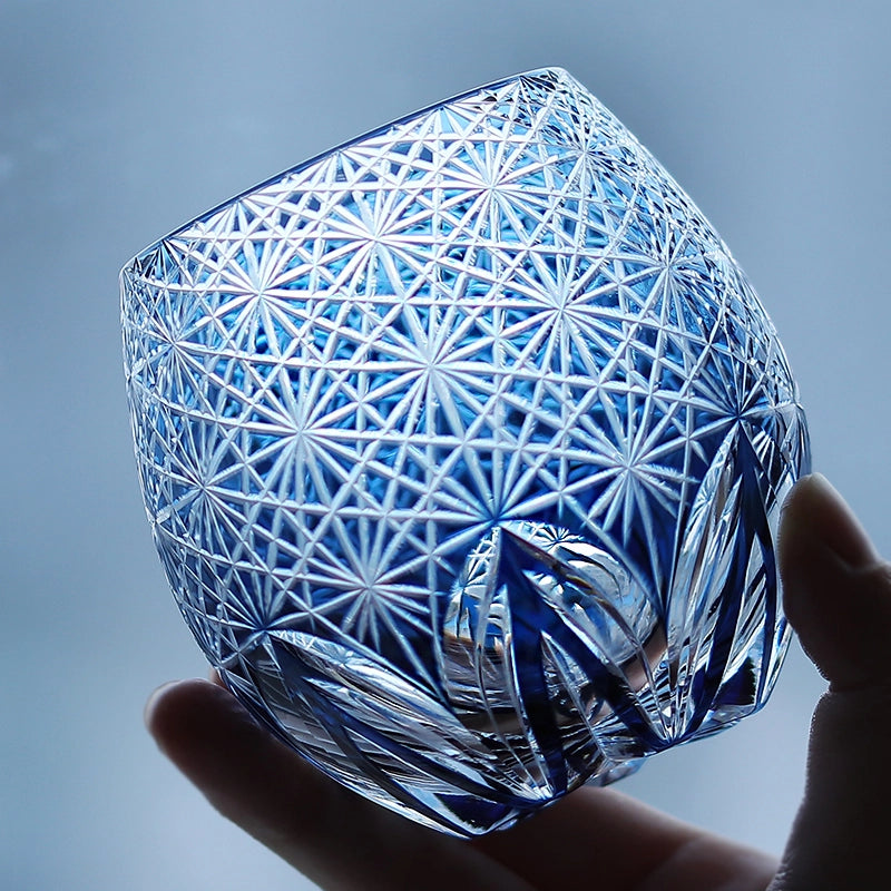Hand holding blue hand cut crystal whiskey glass with geometric starburst pattern
