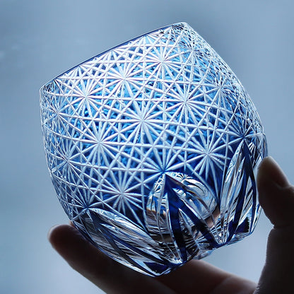 Hand holding blue hand cut crystal whiskey glass with geometric starburst pattern